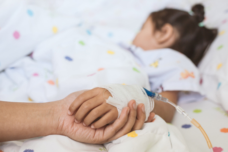 parent holding hand of child in hospital bed